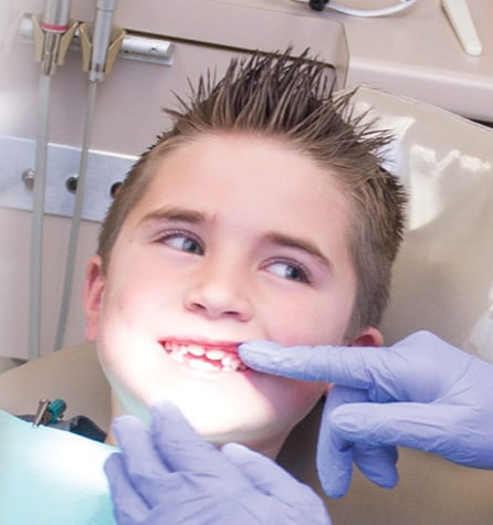 A young boy sitting in a dentist's chair while the dentist examines his teeth.