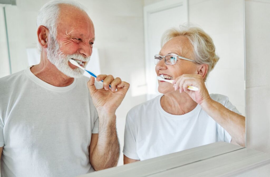 A couple at home cares for their dental implants by brushing their teeth together.