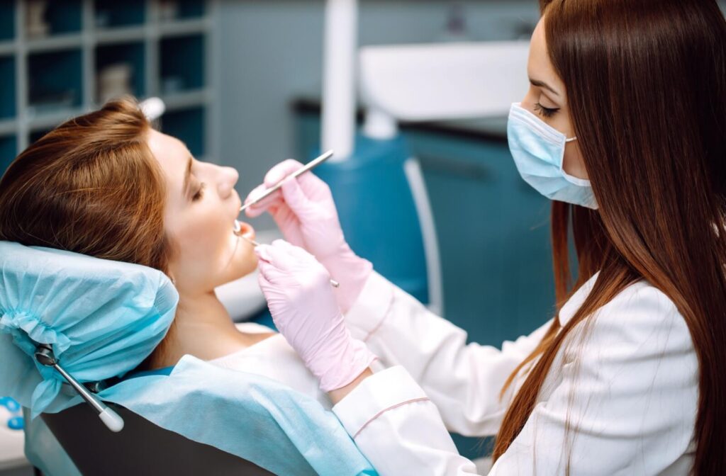 A woman with auburn hair opens her mouth so her dentist can examine her mouth to determine the quality of her dental bridge