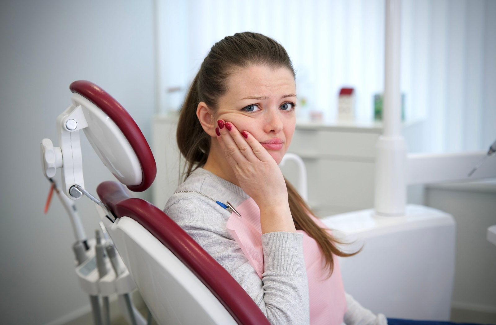 A dental patient holds their hand to their cheek in pain while sitting in the dentist’s chair