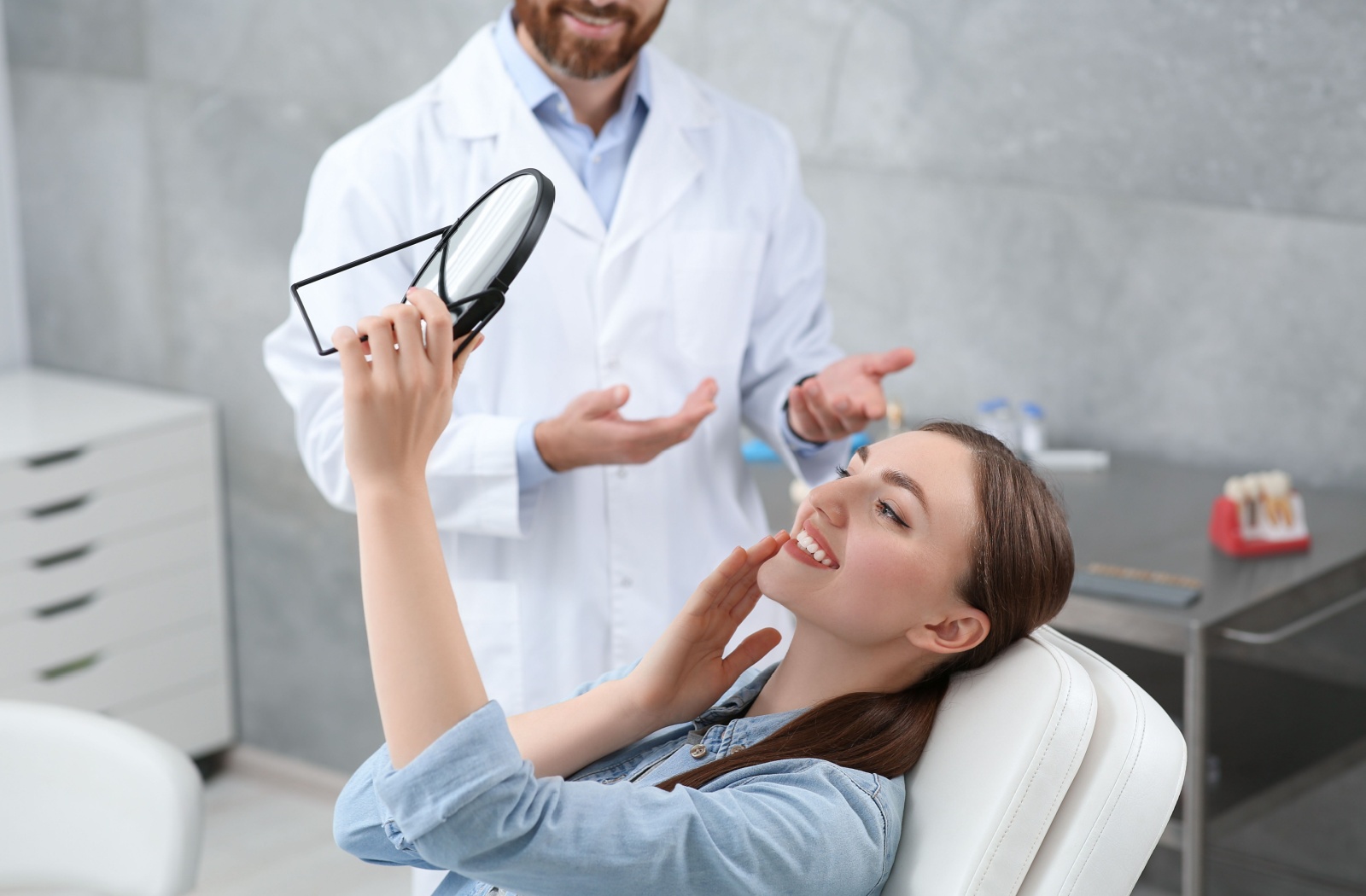 Smiling woman looking at her teeth in a mirror during a dental consultation.