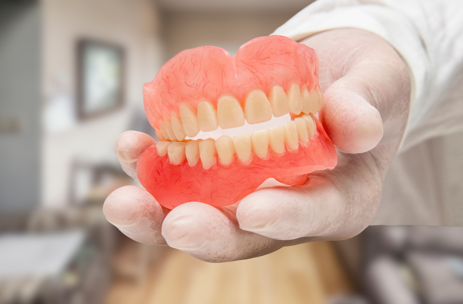 A hand wearing gloves holding a complete set of dentures.