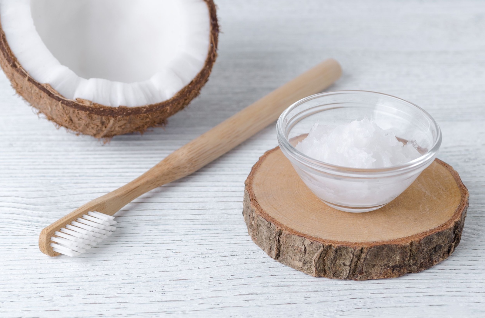 A toothbrush rests between half a coconut and a bowl of coconut oil.
