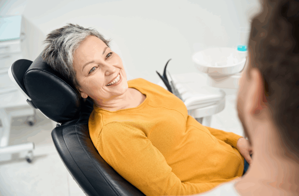 Senior woman smiling in dental chair, speaking to dentist about dentures.