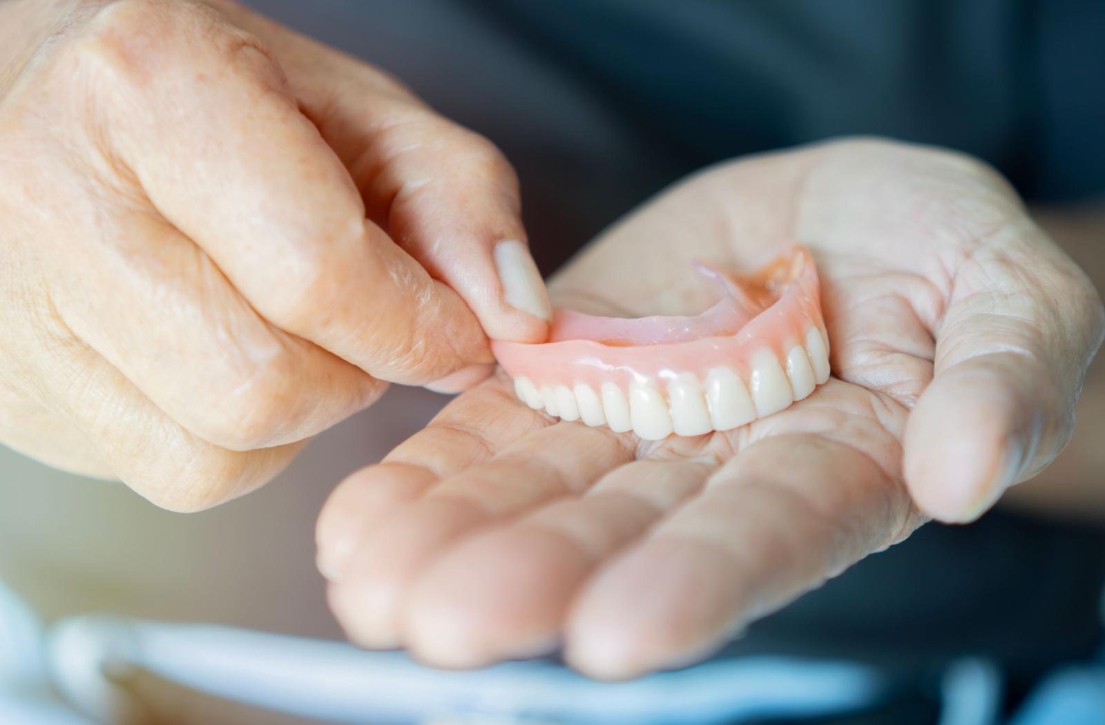 Hands holding a set of dentures, highlighting the importance of proper denture cleaning and daily care.